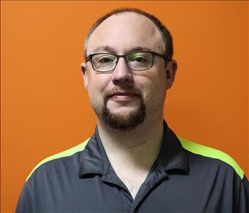 A man in a gray shirt standing in front of an orange background