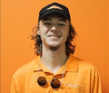 A man in an orange shirt standing in front of an orange background