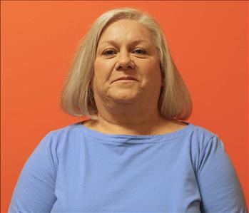 A woman in a blue shirt standing in front of an orange background