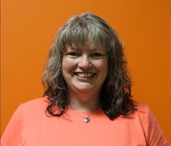 A woman in a coral shirt standing in front of an orange background