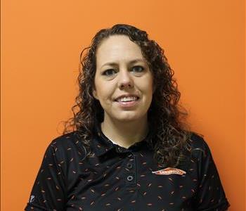 A woman in a black shirt standing in front of an orange background