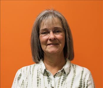 A woman in a white shirt standing in front of an orange background