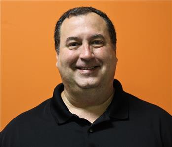 A man in a black shirt standing in front of an orange background