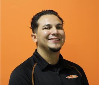 A man in a black shirt standing in front of an orange background