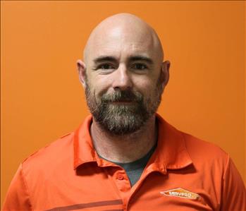 A man in an orange shirt standing in front of an orange background