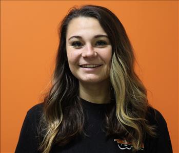 A woman in a black shirt standing in front of an orange background